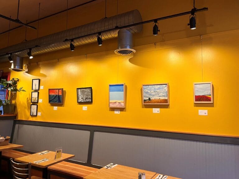 Artist Megan Velthuizen's paintings displayed on the yellow walls of the Harris Avenue Cafe.
