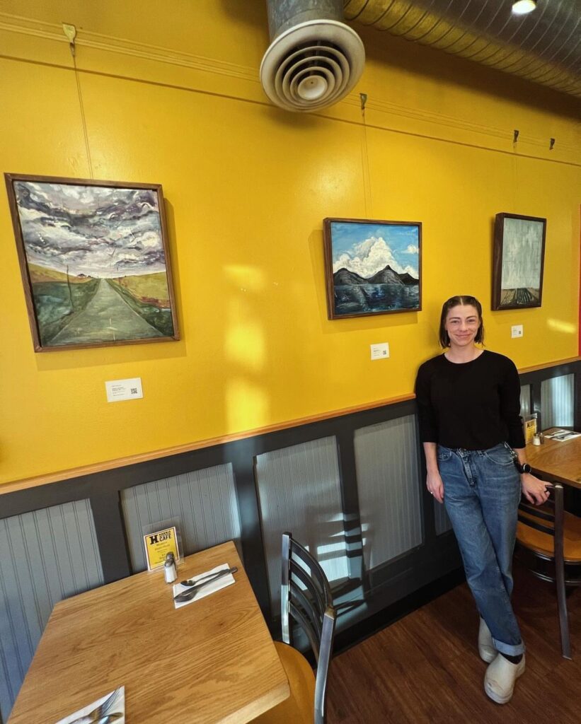Megan Velthuizen stands in front of her paintings hanging on the yellow walls of Harris Avenue Cafe.