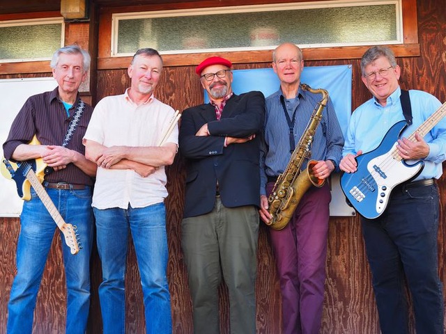 The Atlantics posing for a photo with their instruments against a wooden wall.