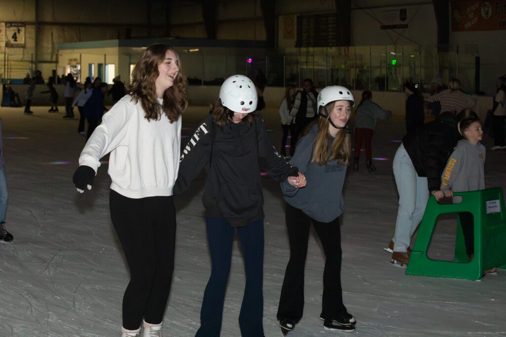 Charlotte Swart, left, Dylan Kubista, middle, and Kate Gasper, right hold hands has the curve around the rink.