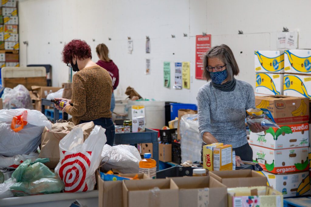 Volunteer Ev Bethke, surrounded by boxes and bags full of food, sorts food at the Bellingham Food Bank while her colleagues do the same nearby.