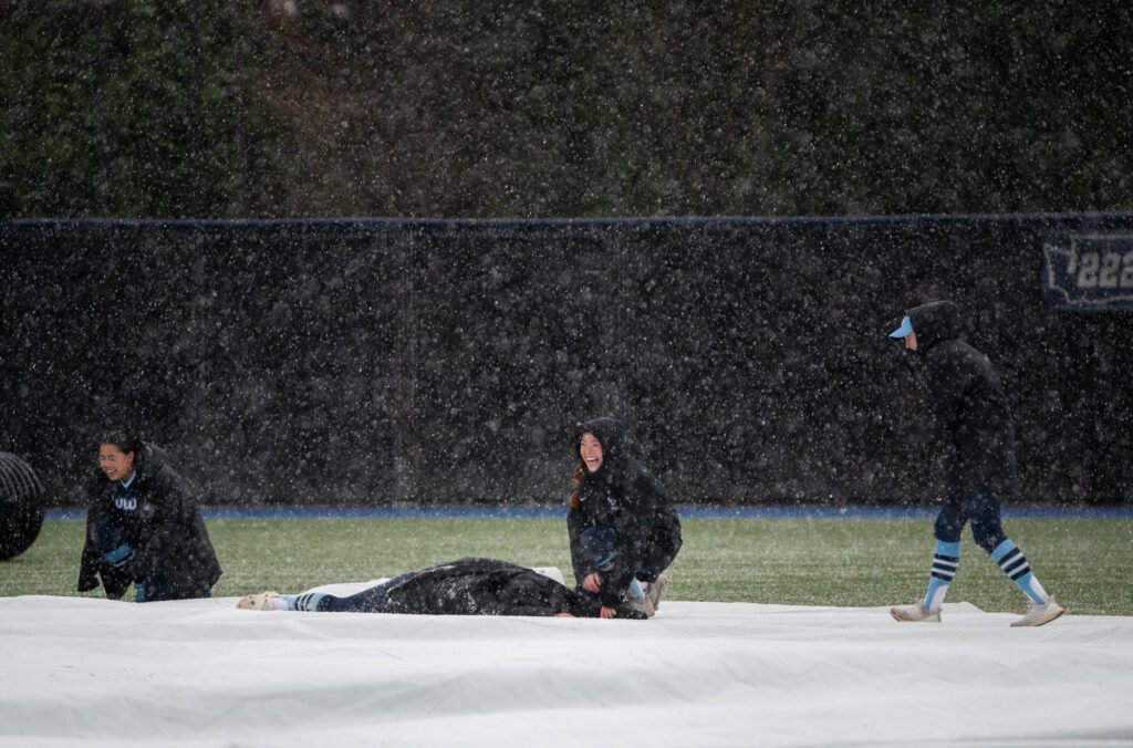 From left, junior infielder Amaya Davis, senior catcher Emily Paulson and sophomore infielder Hailey Rath laugh as junior pitcher Joie Baker slips on the tarp as they cover the infield.