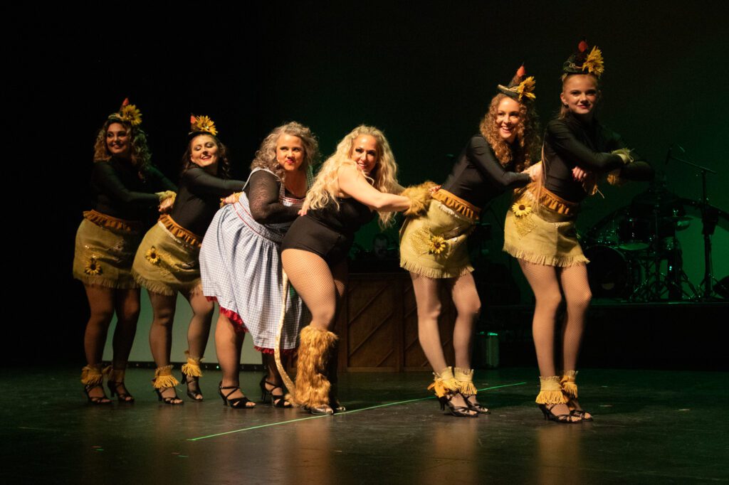 Performers in floral outfits line up with Brie Mueller as Sugar at the center.