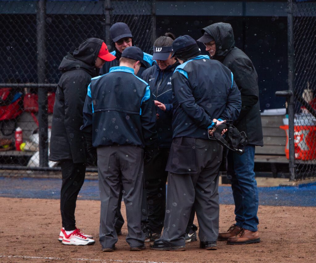 Umpires and a Simon Fraser coach look at Western head coach Sheryl  Gilmore's phone before deciding to cancel the second game of the double header.