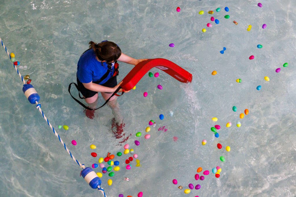 A lifeguard uses a safety float to move eggs apart before the start of an underwater egg hunt.