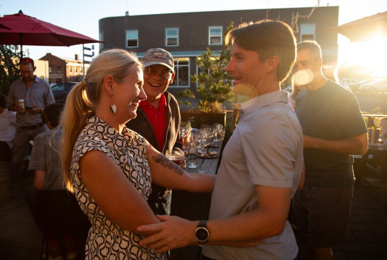 Kim Lund, left, hugs her husband Gil while people around her congratulate her as the setting sun shines on the group.