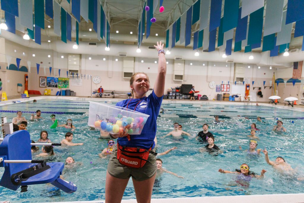 Lifeguard Kate Chapman throws eggs backwards over her head to kids waiting in the pool.