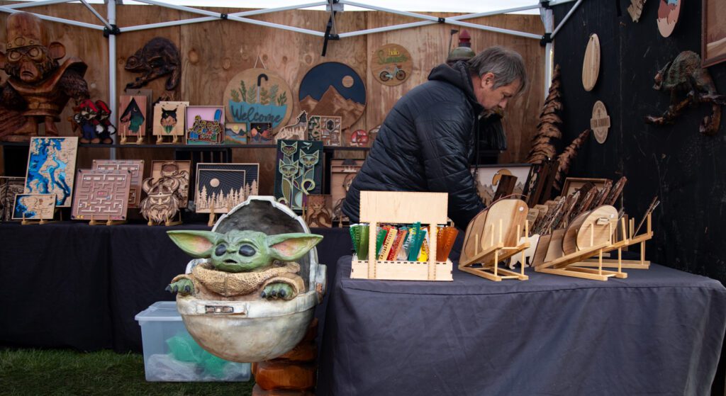Jimmy "Ak Woody" Kitchens organizes his wooden creations at his booth. He creates sculptures with chainsaws, like Grogu, pictured, and the Mandalorian from the TV show "The Mandalorian."