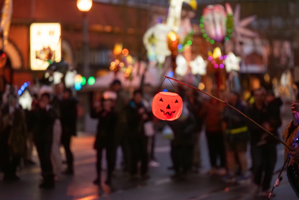 A spectator holds a flashing jack-o-lantern on a stick as the parade goes by.