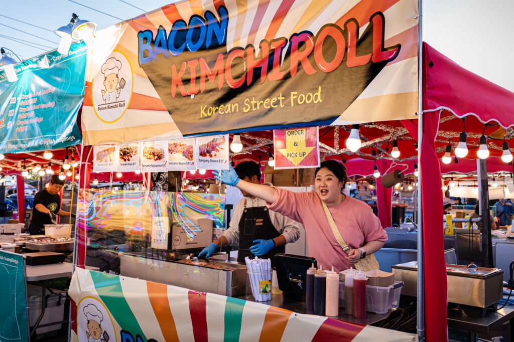 A vendor hawks bacon kimchi rolls to passersby.