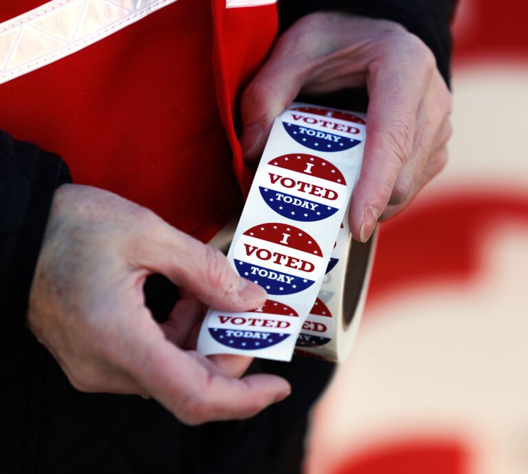 A person unravelling a roll of stickers colored in red, white, and blue labeled 'I voted today'.