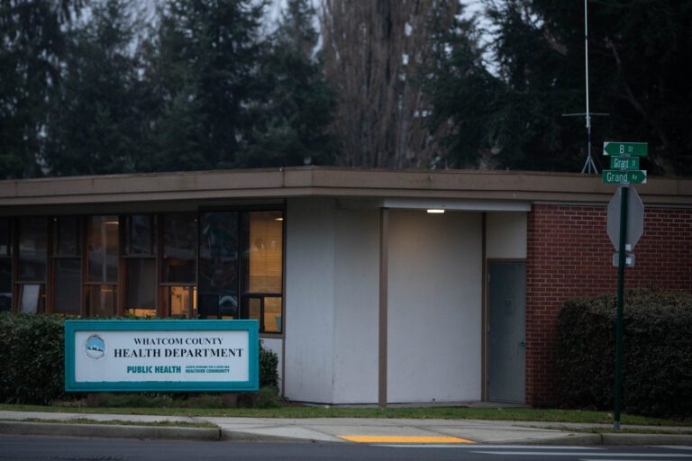 The front of Whatcom County Health Department where a sign is displayed next to the door.