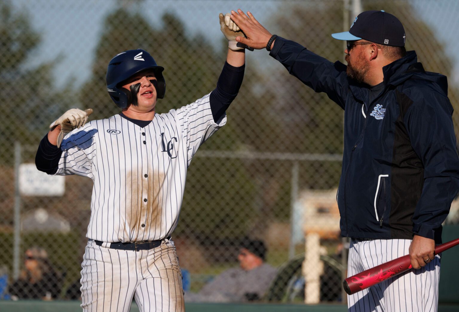 Lynden Christian’s Austin Engels fist-bumps an assistant coach after scoring the tying run Friday, April 12, during an 8-5 home win over Nooksack Valley.