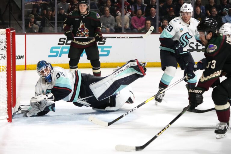 Seattle Kraken goaltender Joey Daccord, left, makes a diving save on a shot by Arizona Coyotes left wing Michael Carcone, right, as Kraken defenseman Vince Dunn (29) and Coyotes center Logan Cooley, back left, look on.