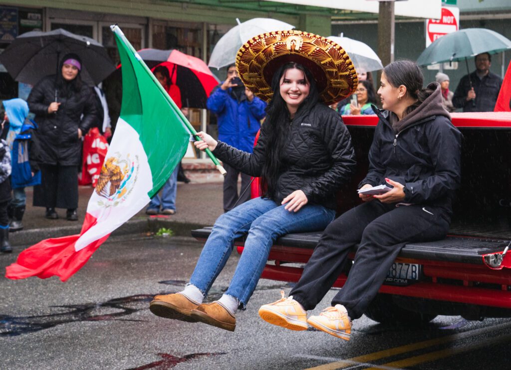 A parader waves the Mexican flag from the back of a truck.