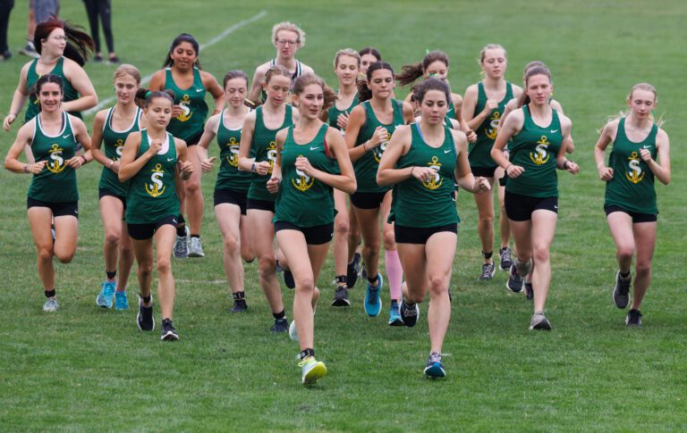 Sehome girls’ cross country participants run across the grassy field, all members wearing their team's signature green tank tops.