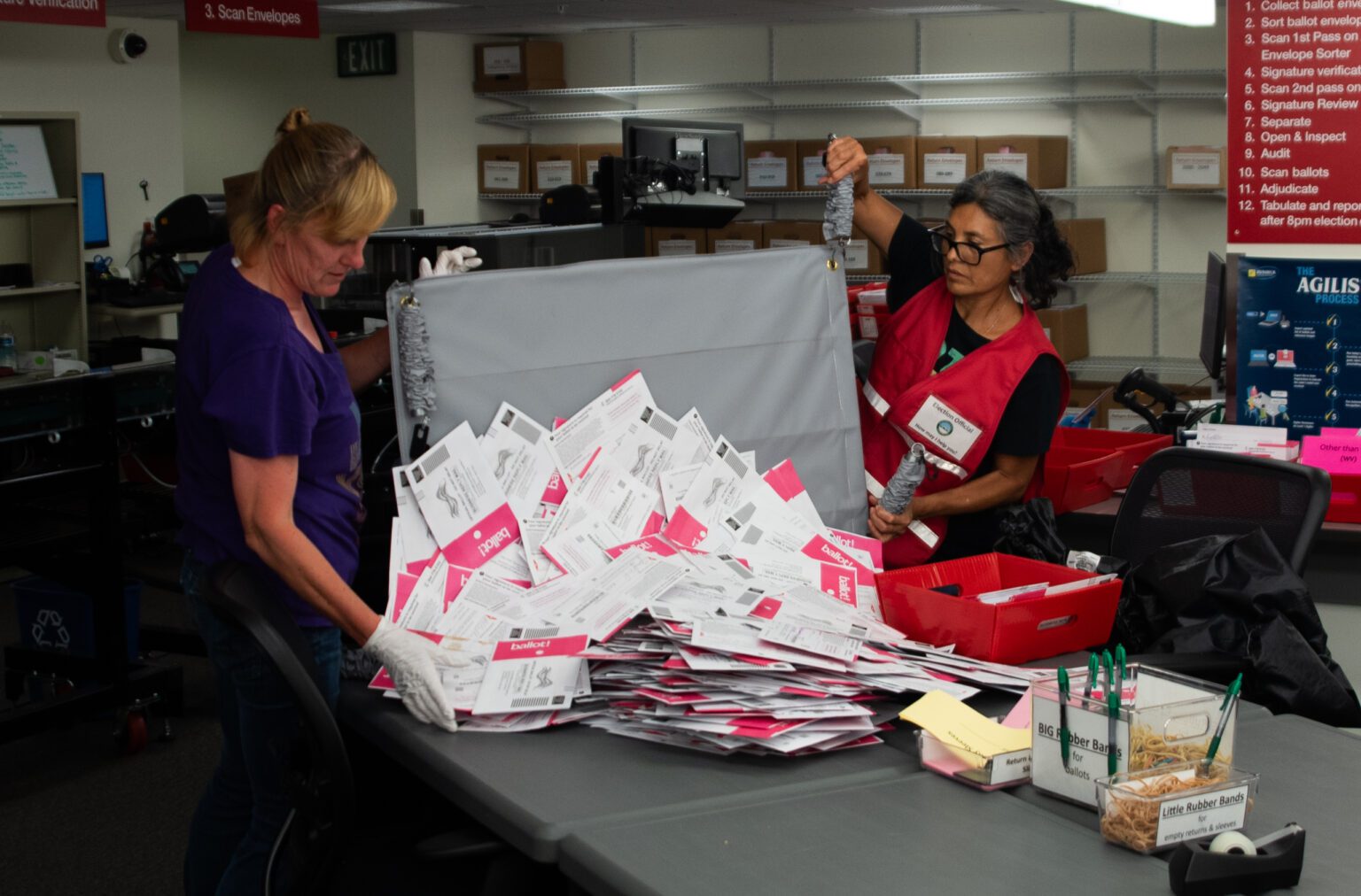 Election Supervisor Amy Grasher, left, and another election official dump a container full of ballots on the table.
