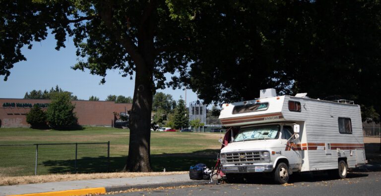 A recreational vehicle, with its window blocked out by cardboard, is parked near Arne Hanna Aquatic Center.