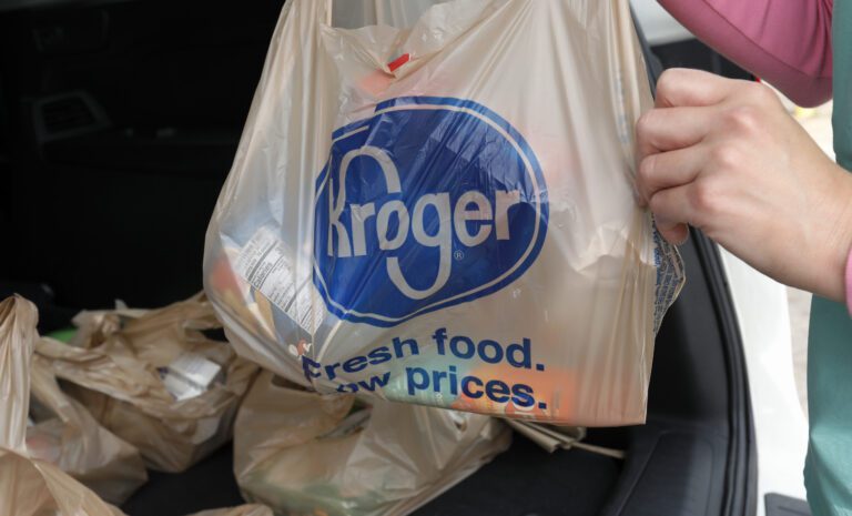A person holds up a Kroger plastic bag filled with various groceries.